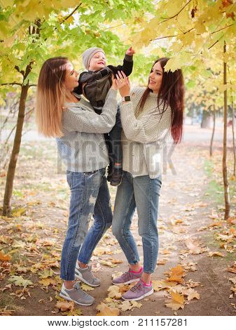 Mom and her son in the autumn in the park holding him in his arms with a girlfriend
