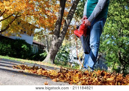 Man working with leaf blower: the leaves are being swirled up and down on a sunny day