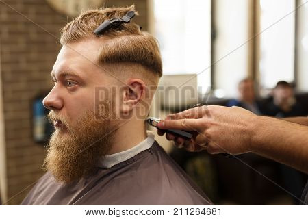 Barber styling beard with trimmer at barbershop, closeup of client's head. Male Barbershop