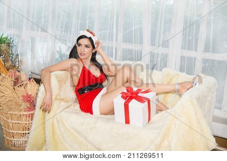 Pretty Asian woman in Santa dresses with gift sit down on the sofa in a room.