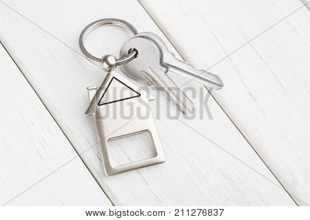 Two steel keys with house shaped trinklet on keyring on white wooden background with copy space. Home key, safety, security, real estate and rent concept