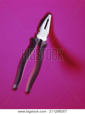 PAIR OF PLIERS CASTING SHADOW ON PINK BACKGROUND