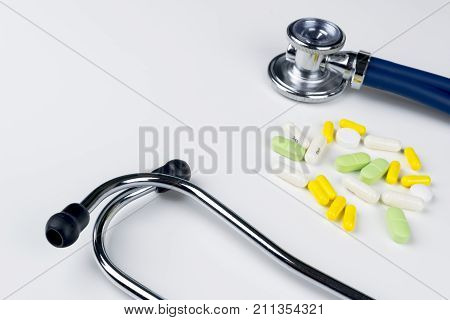 Medical stethoscope lying on white table with pile of pills. Cardiology care health protection prevention and help. Healthy life or insurance concept. EKG ECG stethoscope and different pills.
