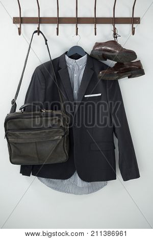 Close-up of blazer, shoes, and bag hanging on hook against white background