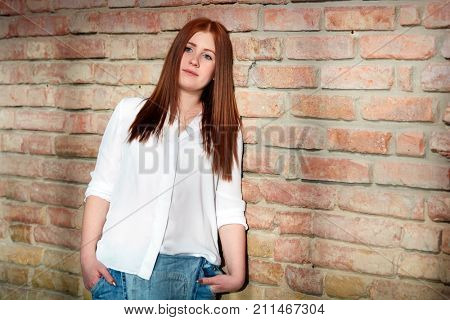 Young ginger girl daydreaming by brick wall.