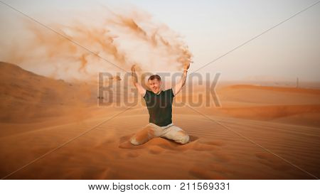 The guy throws sand over himself in the desert. The desert is next to Dubai. UAE