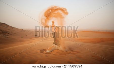 The guy throws sand over himself in the desert. The desert is next to Dubai. UAE