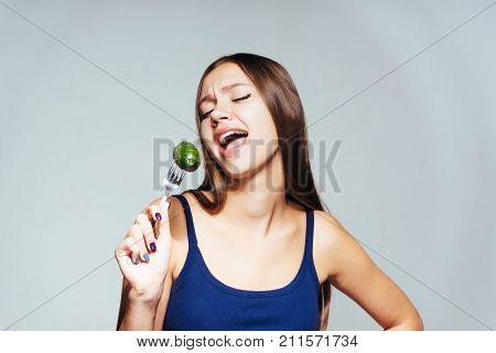 a young funny girl in a blue top wants to lose weight, holds a fork with a cucumber and sings