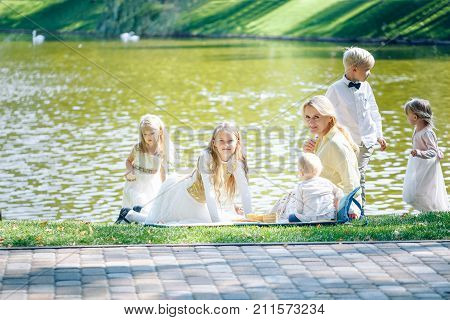 Grandmother and grandchildren enjoying picnic in a park. Grandma playing with children in a sunny summer forest. Summer outdoor fun in the garden. Grandparents and kids on a meadow near water.