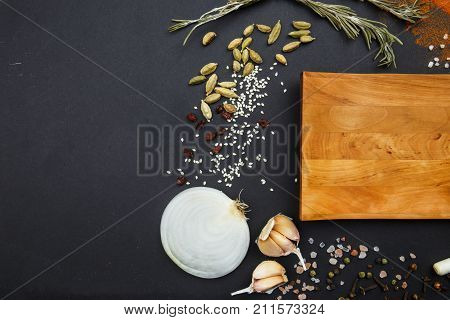 Composition with a cutting board, spices onions, green onions and garlic on a black background. Concept of food, spices, restaurant. Free space for text.