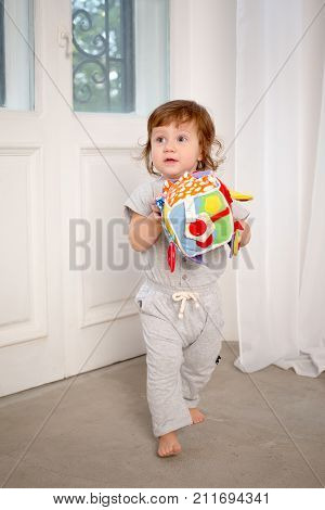 Little curious girl playing with toy on white door background. Home.