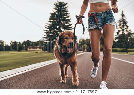 Getting some fresh air. Close-up of young woman running with her dog through the park while spending time outdoors