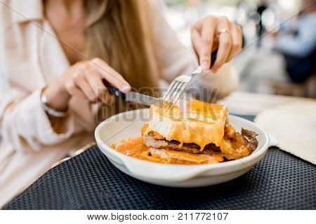 Eating traditional portuguese meat sandwich with tomato sauce called francesinha at the restaurant in Porto city