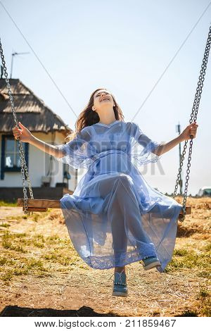 healthy young girl sitting on swing, sweet woman in blue dress have resting in village