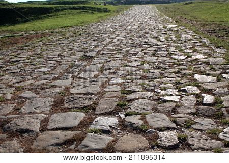 Ancient road paved with cobblestone and going up through hills. Perspective view.