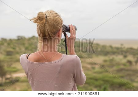 Female tourist looking through binoculars on African safari in Serengeti national park, Tanzania, Afrika.
