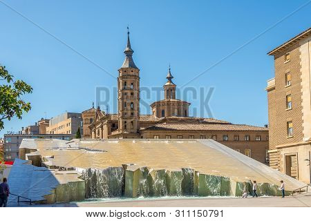 Zaragoza,spain - May 11,2019 - Fountain With Church Of San Juan Panetes At The Pillar Square In Zara