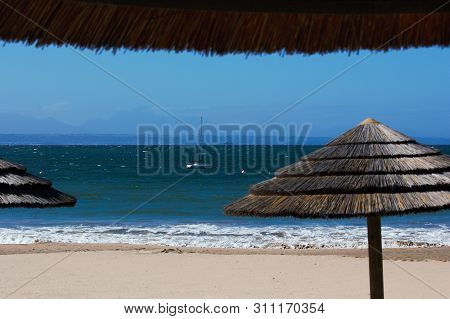 Beach Palapas Overlooking Ocean With Sailboat, Mossel Bay, South Africa