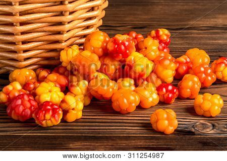 Handful Of Cloudberry Berries Poured From A Small Basket On An Old Wooden Board Close-up