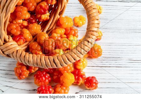 Handful Of Cloudberry Berries Poured From A Small Basket On An White Wooden Board Close-up