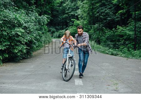 Happy Laughing Father With His Son On A Balance Bike., Family Having Fun Together At The Green Park,