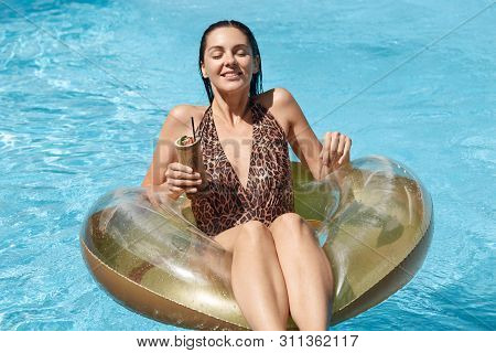Young Woman Enjoying Her Luxury Vacation At Resort, Swimming With Rubber Ring And Cocktail In Hand I