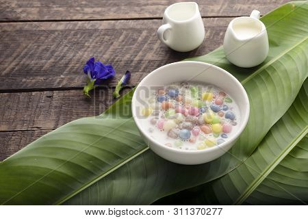 Thai Sweets And Colorful Ball Flour In A White Cup On A Banana Leaf, Coconut On An Old Wooden Table 