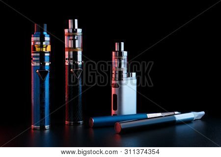 Electronic Cigarettes Or Vaping Devices On Black Background. Toned Light