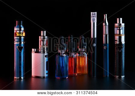 Electronic Cigarettes And Bottles With Vape Liquid On Black Background. Toned Light