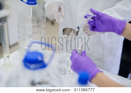 Close Up Of Technologist`s And His Asisstant Hands Pouring Chemical With Syringe Into Chemical Ballo