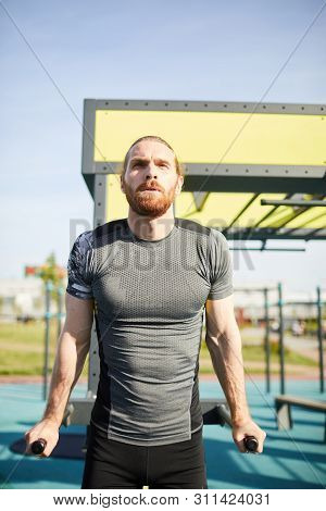 Concentrated Tenacious Man In Sportswear Exhaling While Doing Pull-ups On Bars Outdoors
