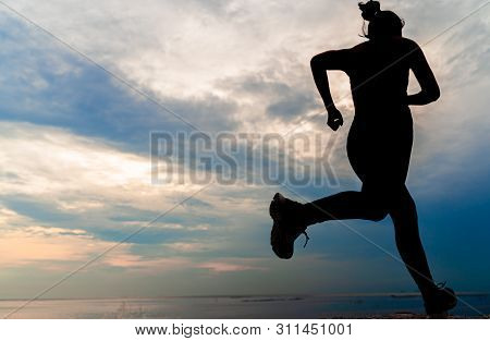 Silhouette Woman Running On The Beach At Sunset. Girl Jogging Workout In Seaside