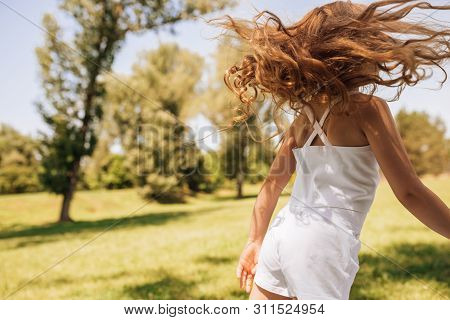 Rear View Image Of Adorable Little Girl With Long Blond Hair Dancing At Nature Background. Happy Chi