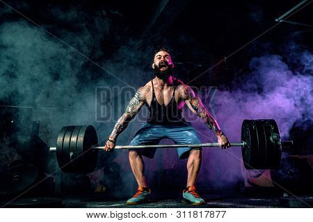 Muscular Bearded Tattoed Fitness Man Doing Deadlift A Barbell Over His Head In Modern Fitness Center
