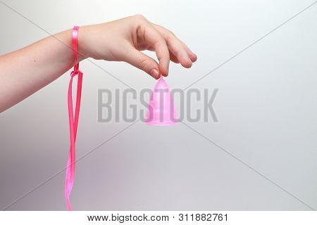 A Woman Holds A Menstrual Cup In Her Hand On A Pink Background. The Concept Of Women's Health, Hygie
