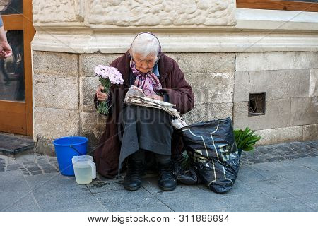 Lviv, Ukraine - 26 May 2019: Elderly Woman Selling Flowers. Old Woman Sitting On Street And Reading 