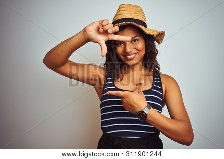 Beautiful transsexual transgender woman wearing summer hat over isolated white background smiling making frame with hands and fingers with happy face. Creativity and photography concept.