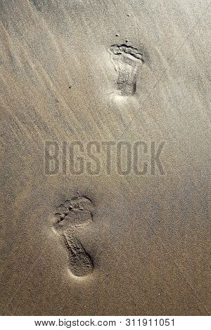 Human Barefoot Footprints Dissapearing In Brown Yellow Sand Beach Background, Summer Vacation Or Cli