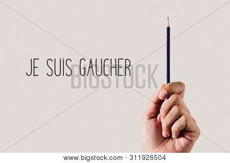 closeup of a young left-handed man with a pencil and the text je suis gaucher, I am left-handed written in French, on an off-white background