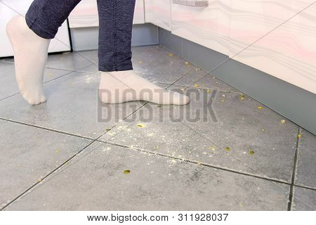 Woman On The Dirty Floor In The Kitchen. Leftovers And Crumbs On The Kitchen Floor. Legs Close-up