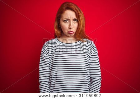 Young redhead woman wearing strapes navy shirt standing over red isolated background depressed and worry for distress, crying angry and afraid. Sad expression.