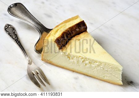 Cheesecake Slice On White Plate On Vintage Cake Server With Cake Fork On Marble Plate.