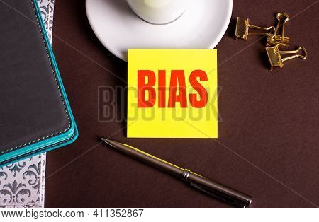 The Word Bias Written On Yellow Paper On A Brown Background Near A Coffee Cup And Diaries