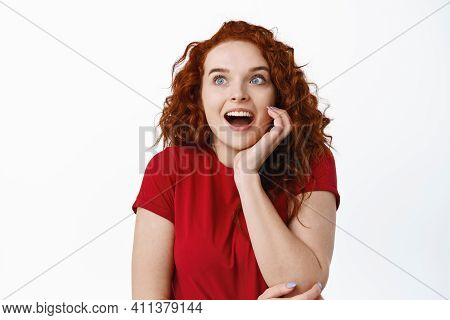 Portrait Of Fascinated Young Woman With Red Curly Hiar, Gasping Amazed, Staring Excited At Left Side