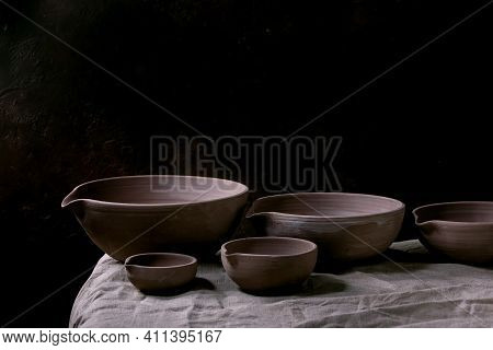 Set Of Craft Handmade Unglazed Dark Clay Pottery Bowls With Spout On Table With Dark Background.