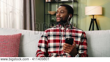 Portrait Of Handsome Cheerful Young African American Guy Enjoying Music In Earphones On Cellphone Li