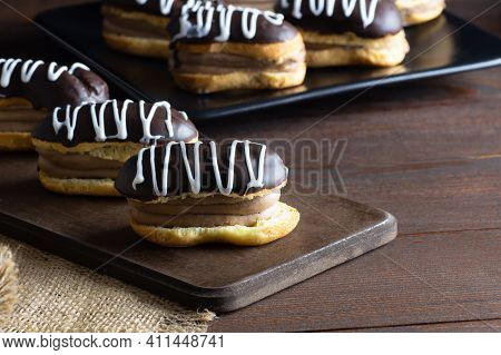 Eclairs With Black Chocolate And White Chocolate With Custard On Rustic Table. Traditional French De