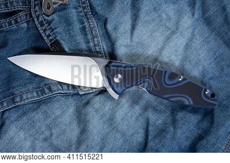 A Casual Folding Knife Rests On Jeans. Knife With A Blue Handle.