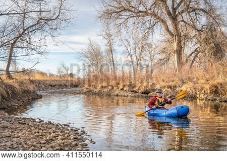 senior male  is paddling an inflatable packraft on a river in early spring spring - Poudre River in northern Colorado