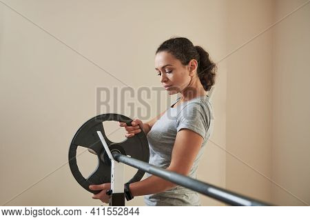 Attractive Young Woman Putting Metal Disk On Barbell Before Exercising Heavy Barbell Training. Fit W